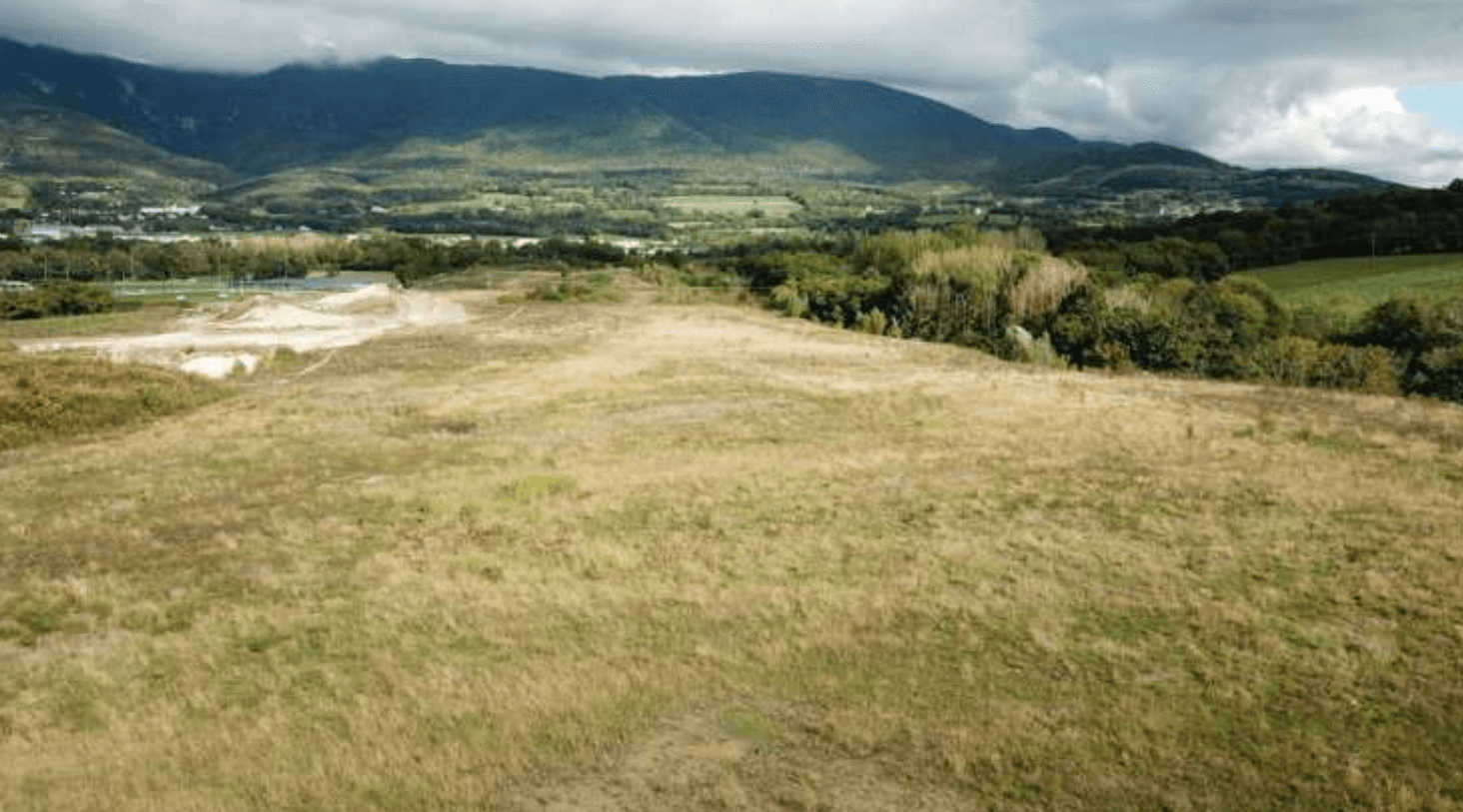 Photo par drone du site actuel : friche sèche et remaniée, la chaîne du Jura en arrière-plan